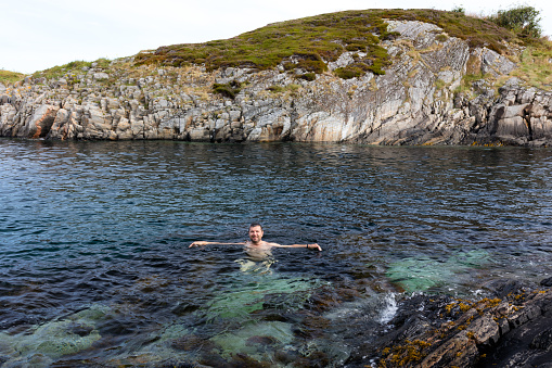 A smiling man in the water between the cliffs in the Norwegian Sea