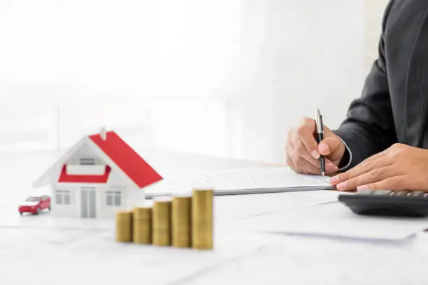 Photo of Businessman signing document with money and house model on the table