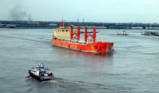 A Fire Boat approaches a Bulk Carrier Cargo Ship as Tugboats head down river in the busy river port of New Orleans