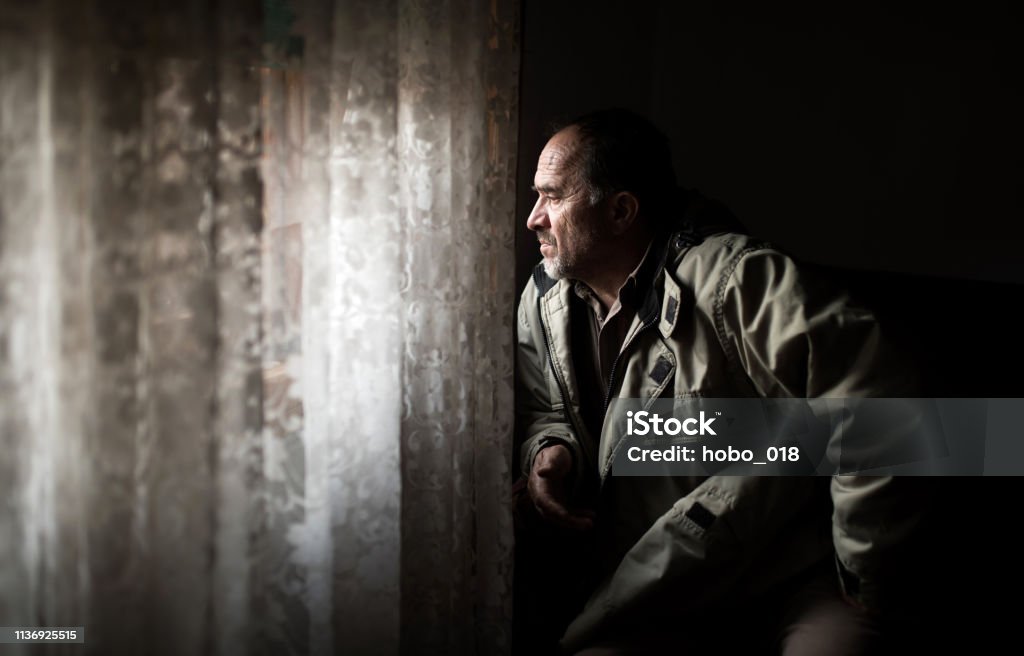 Middle Age Man looking Through Window Middle Age Man sitting at home, next to the window, looking through window, waiting for someone Depression - Sadness Stock Photo