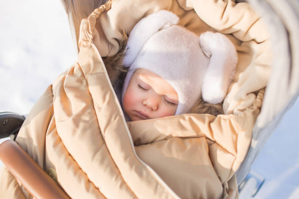 Little baby in cap of hare sleeps in baby carriage outside Little baby in cap of hare sleeps in baby carriage outside baby stroller winter stock pictures, royalty-free photos & images