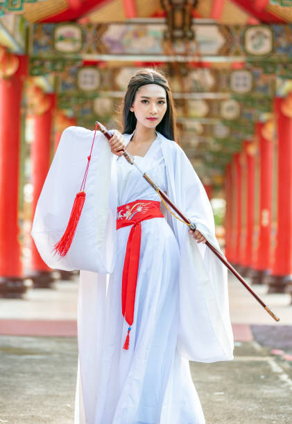 Beautiful Chinese woman with a traditional suit with a sharp sword in her hands, Beautiful and belligerent face, Young woman with a samurai bushido katana sword stock photo