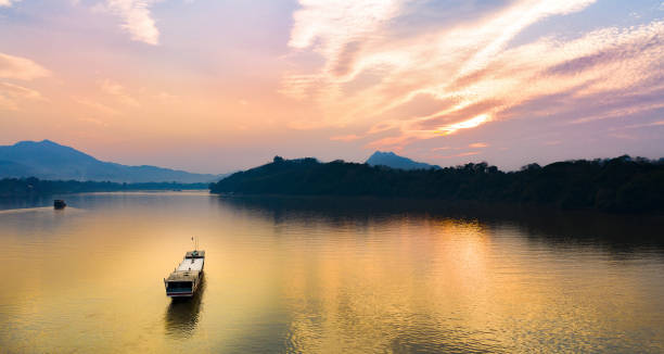 View from above, stunning aerial view of a tourists boat sailing along the Mekong river at sunset. Sunset Cruise is a slow-boat cruise along the Mekong river and is one of the most famous tourist attractions of Luang Prabamg, Laos. stock photo
