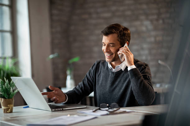 businessman talking on cell phone Happy businessman communicating over mobile phone and working on laptop while being at work. ringing stock pictures, royalty-free photos & images