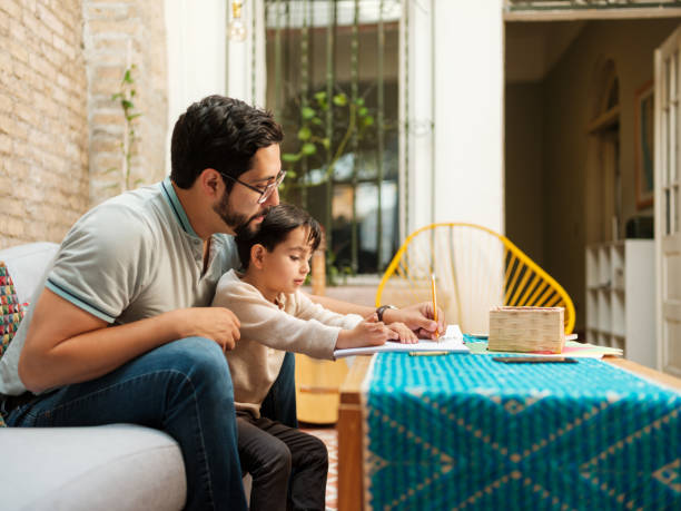 istock Mexican father sitting on sofa with son and writing on notebook 1136937761