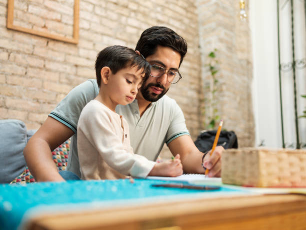 Mexican father and young son drawing on notebook at home stock photo