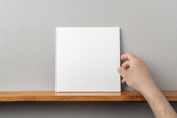 istock man's hand hold white square notebook on bookshelf 1136939076