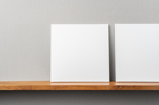 Design concept - front view of 2 square white notebook on bookshelf and grey wall for mockup