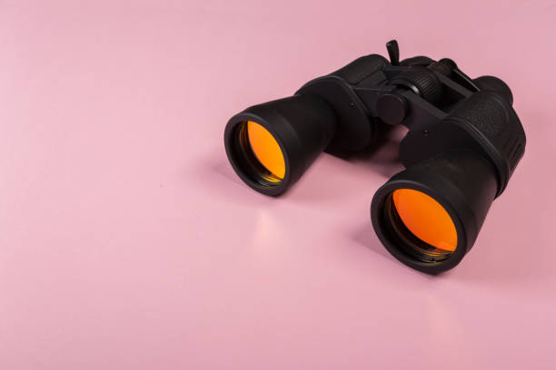 istock Black binoculars with orange lens on pink background 1136943966