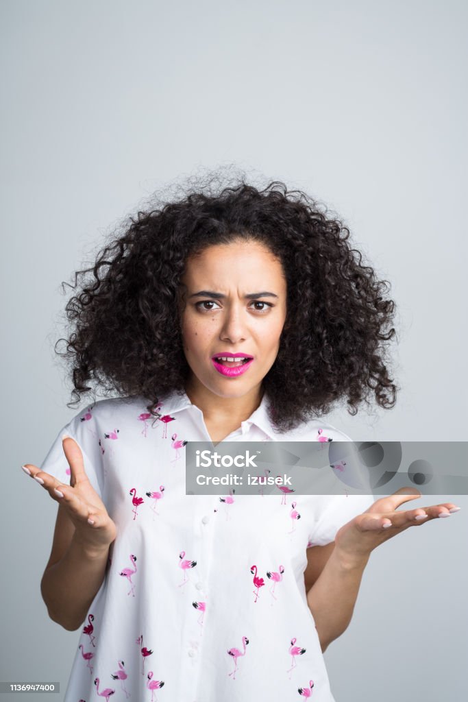 Woman looking really annoyed Portrait of curly haired young woman looking annoyed against gray background 20-24 Years Stock Photo