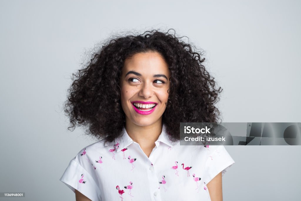 Smiling woman looking away at copy space Close up of smiling mixed race woman with curly hair looking away at copy space on gray background Women Stock Photo