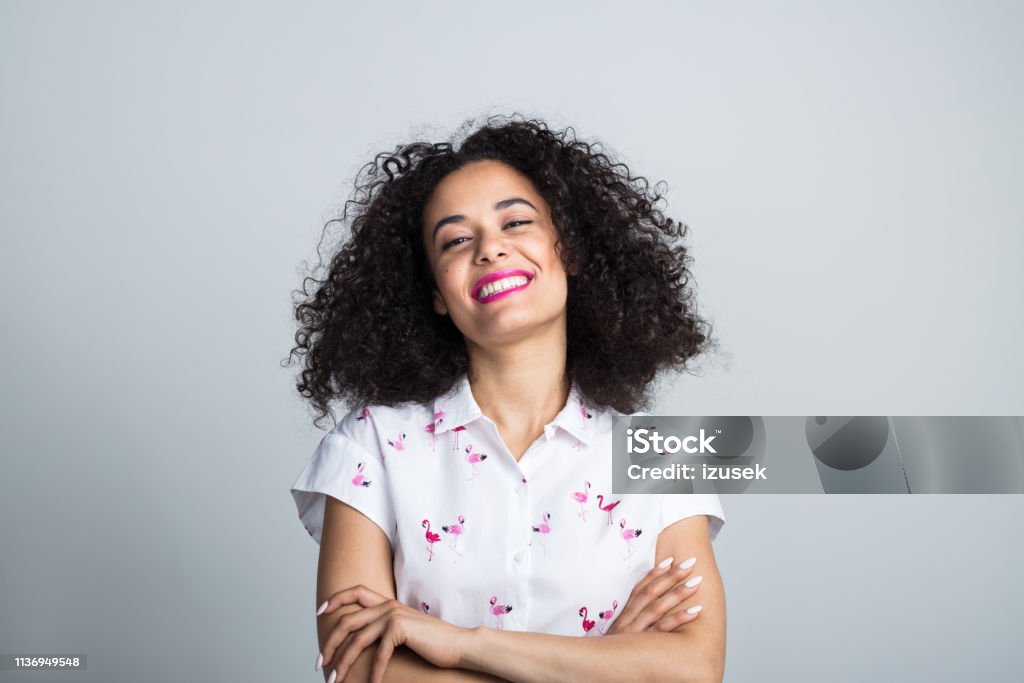 Attractive young woman looking confident Portrait of attractive young woman with curly hair standing with her arms crossed on gray background Women Stock Photo