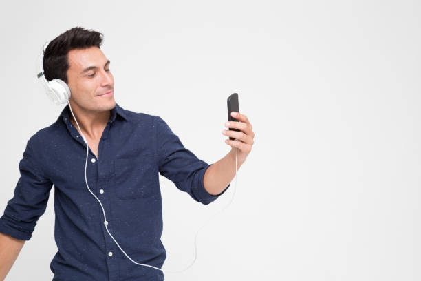 guapo joven caucásico escuchando música con auriculares en el teléfono inteligente, adolescente disfrutando del mejor servicio de streaming de música de gráficos en el sitio web con su lista de reproducción en móvil - samba dancing audio fotografías e imágenes de stock