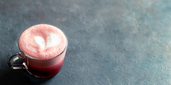 Trendy drink: pink red velvet latte. Beetroot cappuccino or latte in glass cup on black background. Copy space for text. Banner