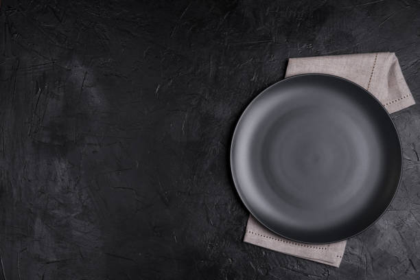istock Black plate, linen napkin on black stone table top view. Table setting. 1136963207