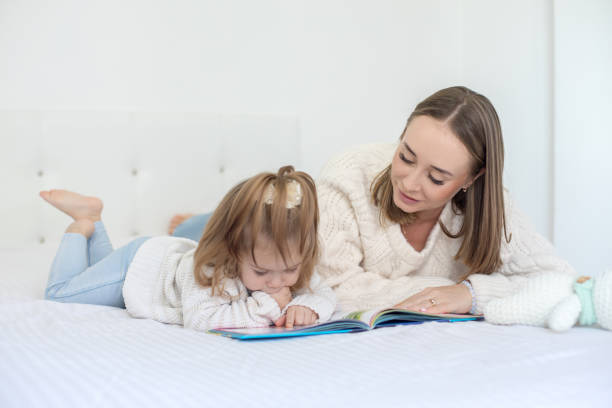 istock Mother and daughter reading book on bed 1136967511