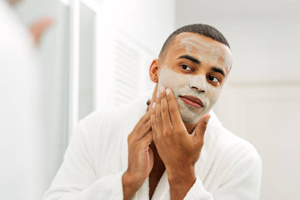 istock Man looking in the mirror with white clay mask on his face 1136973692