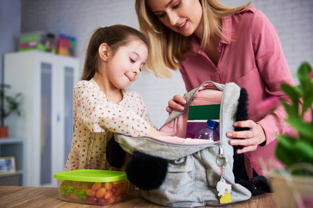 学校のためのバックパックをパッキング若いママと娘 - lunch box ストックフォトと画像