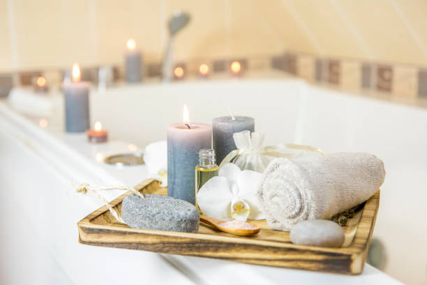 candles and spa essentials on wooden tray in bathroom, essential oil, bath salt on wooden spoon, pumice stone, towel, sea stone, white orchids. spa products set conception. - beauty spa spa treatment health spa orchid imagens e fotografias de stock