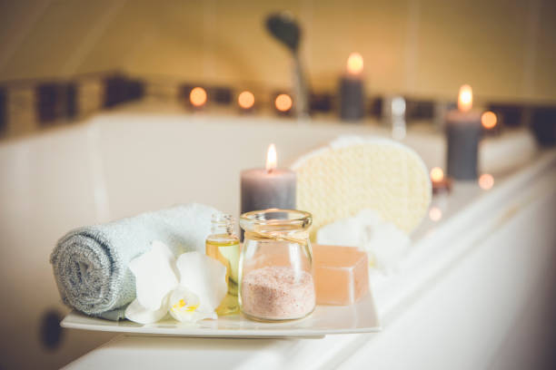 white ceramic tray with home spa supplies in home bathroom for relaxing rituals. candlelight, salt soap bar, bath salt in jar, massage, bath oil in bottle, blue rolled towel, natural sponge. - soap body imagens e fotografias de stock