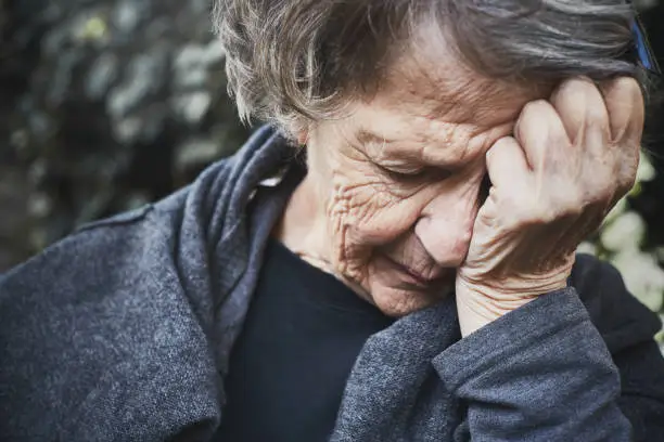 An old woman looks miserable and exhausted, he head in her hands.