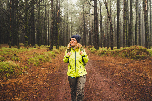 Cheerful beautiful caucasian middle age woman doing trekking outdoor activity in the forest ina rainy day - adventure lifestyle for people love freedom and independence - beautiful nature concept