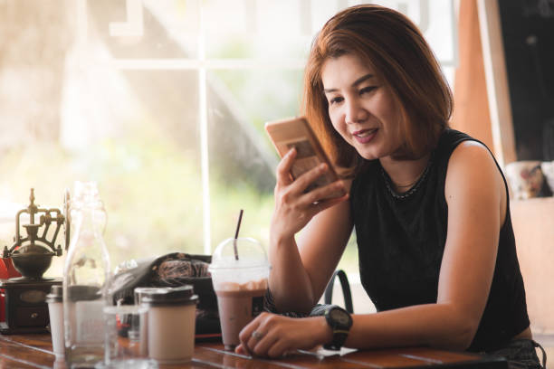 istock Asian woman drinking coffee and using smart phone in cafe. 1136982088