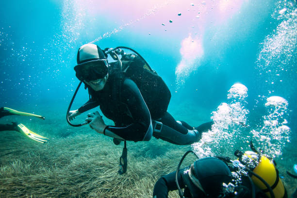 Scuba diver exploring sea bottom Scuba diver looking at camera and smiling while exploring sea bottom covered with high grass around the reef. parga greece stock pictures, royalty-free photos & images
