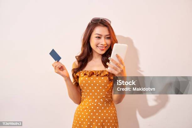 Portrait Of A Happy Girl Holding Mobile Phone And A Credit Card Isolated Over Biege Background Stock Photo - Download Image Now