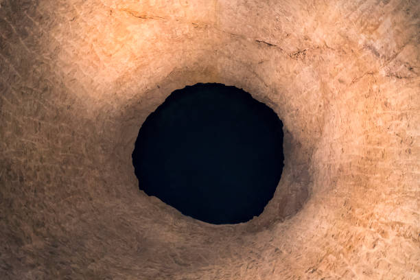 the black round hole in cracked rock crevice. abstraction. fathomless pit of natural origin. bottomless well. black uneven eye in yellow rock. mining. natural borewell. - dirty pass imagens e fotografias de stock