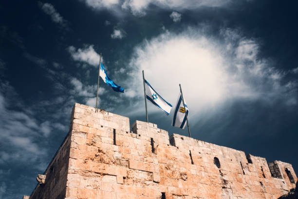 istock Three flags on Jerusalem old tower walls against the dark blue sky and big white cloud. Official symbols of Israel. History, culture and religion of the Jewish people. The modern State of Israel. 1136988856