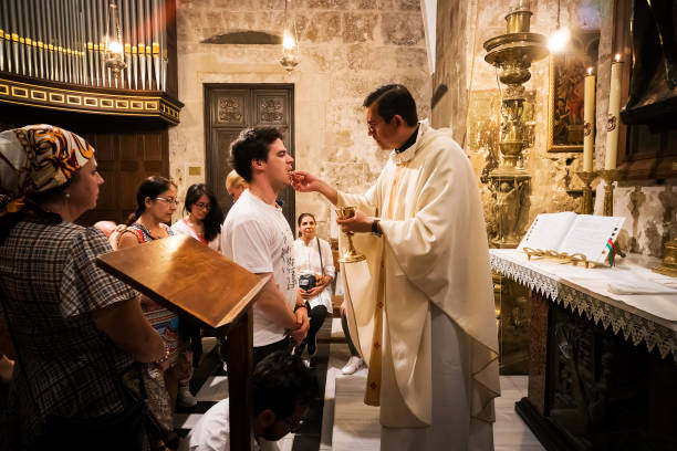 sacerdote de la iglesia del santo sepulcro da la santa comunión al hombre fiel con otros creyentes esperando su turno. jerusalén, israel, 24 de octubre de 2018. - consecrated fotografías e imágenes de stock