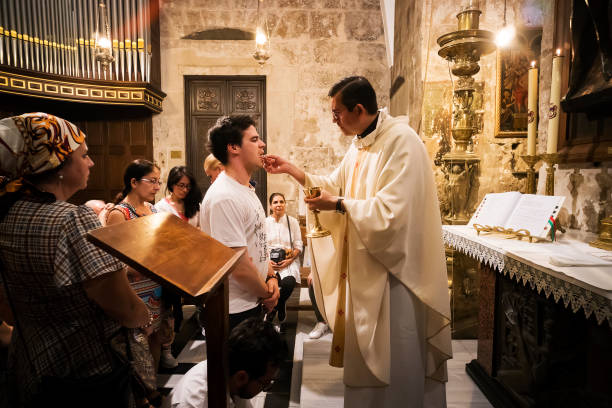 Priest of the Church of Holy Sepulchre gives holy communion to faithful man with other believers waiting for their turn. Jerusalem, Israel, October 24, 2018. Priest of the Church of Holy Sepulchre gives holy communion to faithful man with other believers waiting for their turn. Jerusalem, Israel, October 24, 2018 liturgy photos stock pictures, royalty-free photos & images