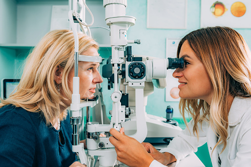 Optician, test and eye exam or care of a woman or customer for vision, eyesight and lens. Optometrist and person at machine or light for healthcare consultation for optometry or ophthalmology service