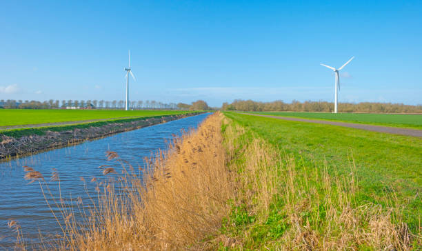 istock Canal in a field below a blue sky in winter seen from a dike 1136992235