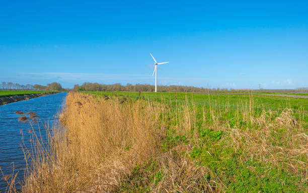 istock Canal in a field below a blue sky in winter seen from a dike 1136992358