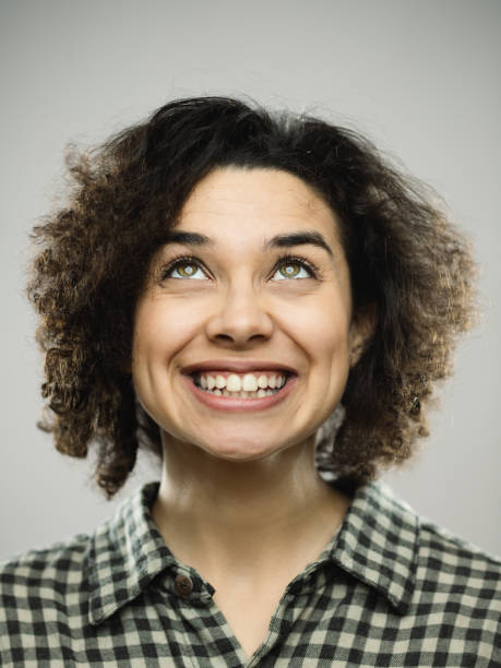 Studio portrait of young happy woman with excited expression looking up Close-up portrait of young caucasian happy woman with excited expression looking up. Vertical shot of hispanic real people laughing and observing with long curly hair and green eyes. Photography from a DSLR camera. Sharp focus on eyes. formal portrait photos stock pictures, royalty-free photos & images