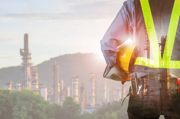 Double exposure of engineer behind with overload tool holding yellow helmet for safety of the workers, Blurred Oil refinery background.