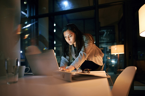 Shot of a young businesswoman using her laptop while working late at the office