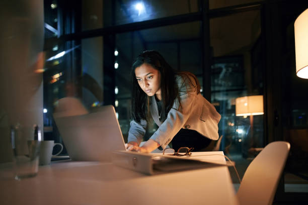 Downloading the last file and then I'm done! Shot of a young businesswoman using her laptop while working late at the office persistence stock pictures, royalty-free photos & images