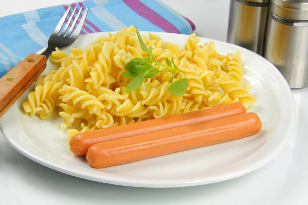 sausages and spaghetti in white plate on dark wooden background.