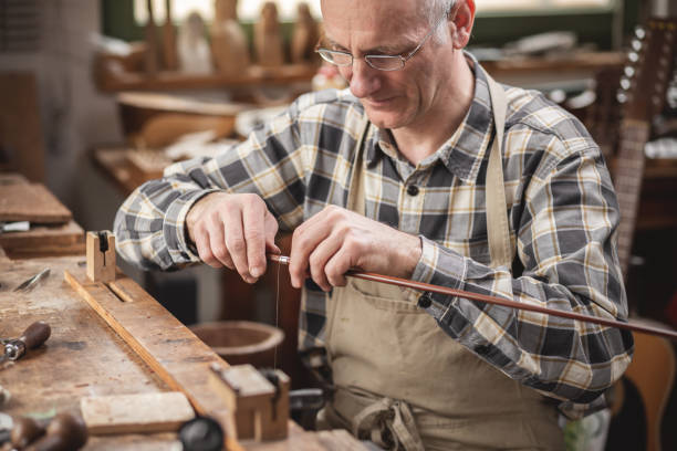 istock Mature instrument maker inside a rustic workshop is winding a wire around a violin bow 1136997220