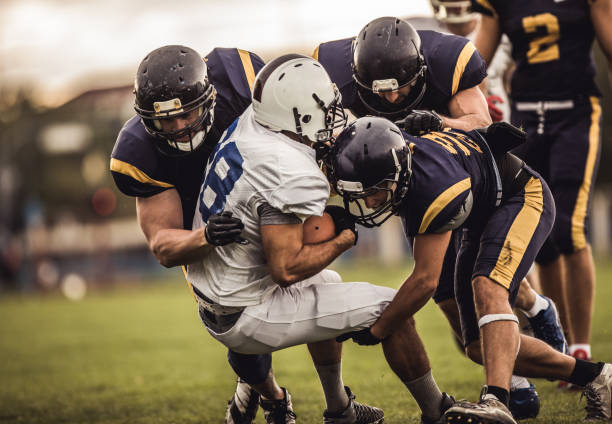 Blocking an offensive player! American football players tackling opposite's team quarterback during the match. match sport stock pictures, royalty-free photos & images