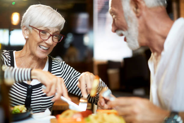 Elderly couple sharing food while dining together in a restaurant Senior couple sharing food and having a good time together in a restaurant. brunch photos stock pictures, royalty-free photos & images