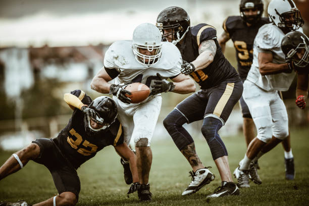 Determined American football player passing through defense for a touchdown. Large group of American football players in action during the match on playing field. Touchdown stock pictures, royalty-free photos & images
