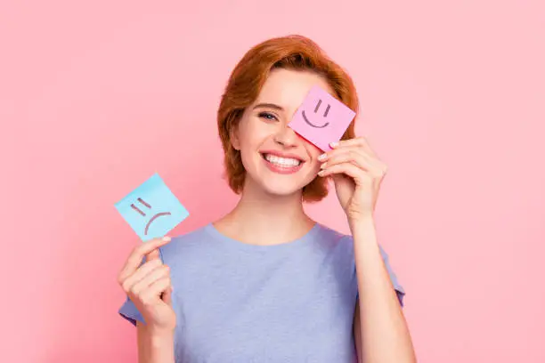 Close-up portrait of her she nice cute charming attractive cheerful girl wearing casual blue t-shirt holding in hands two draw notes positive good choice isolated on pink pastel background.