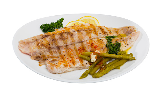 Roasted perch fish fillet served with pickled asparagus and parsley. Isolated over white background