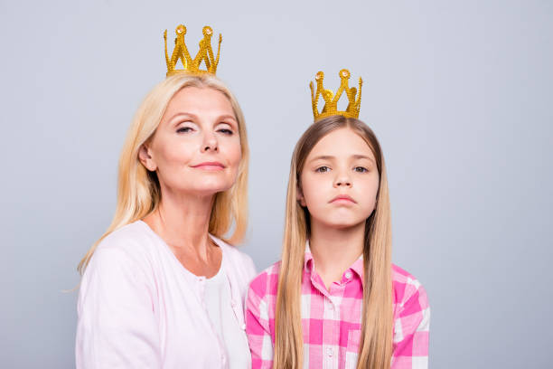 Close up photo two blond haired she her granny little daughter weekend crowns head command order expression haughty wear pink plaid checkered shirt sweater pullover isolated light grey background.