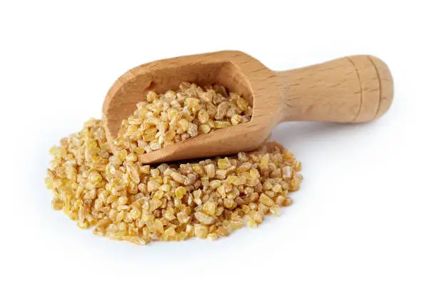 Uncooked raw bulgur wheat grains in wooden scoop isolated on white background