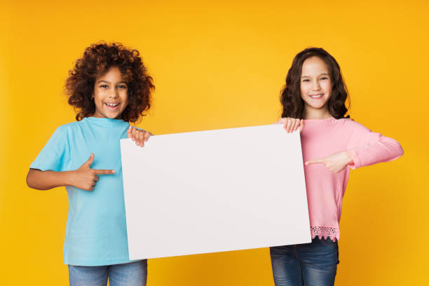 istock Happy girls showing blank board and pointing on it 1137013302